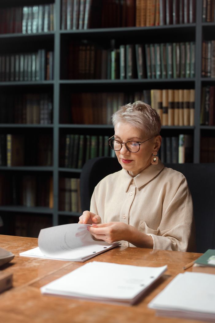 services-01 Elderly woman analyzing scripts in a library, highlighting expertise.